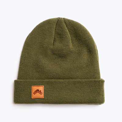 A soft moss green recycled acrylic 6 panel beanie with a custom ALDRI SUR leather logo patch square stitched to the bottom left fold