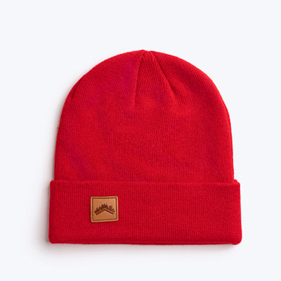 A soft spice red recycled acrylic 6 panel beanie with a custom ALDRI SUR leather logo patch square stitched to the bottom left fold